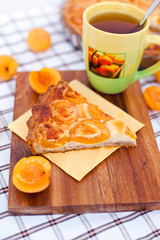 Piece of apricot tart on the wooden board with cup of tea