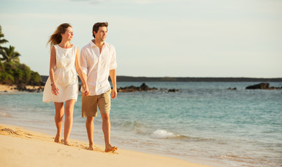 Young couple in love walking on the beach at sunset
