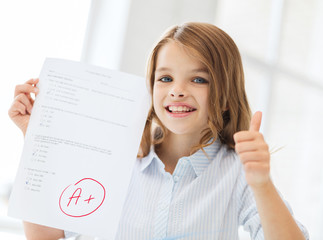 smiling little student girl with test and A grade