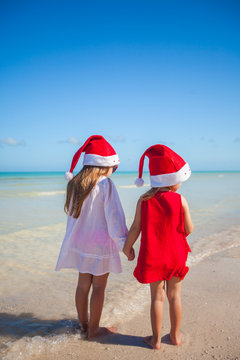 Back view of Little cute girls in Christmas hats on beach