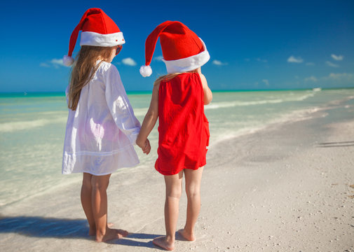 Little cute girls in Christmas hats on beach