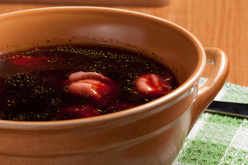 Red borscht with ravioli on a wooden board.