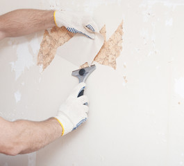 Hand removing wallpaper from wall