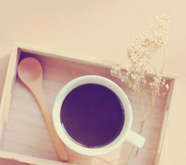 Black coffee and spoon on wooden tray with dried flower, retro f
