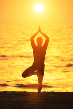 Man in yoga tree pose on sunset ocean beach