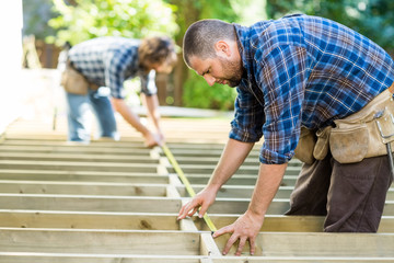 Carpenters Measuring Wood With Tape At Construction Site