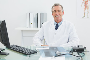 Smiling confident male doctor at desk in office