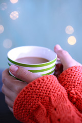 Hands holding mug of hot drink, close-up, on bright background