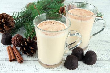Cups of eggnog with fir branches on wooden background