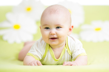 baby girl lying on green meadow among daisy