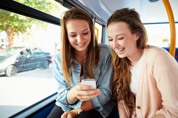 Two Young Women Reading Text Message On Bus - obrazy, fototapety, plakaty