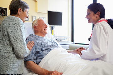 Female Doctor Talking To Senior Couple In Hospital Room