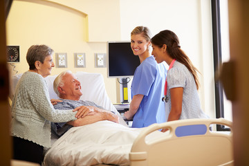 Medical Team Meeting With Senior Couple In Hospital Room