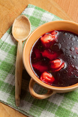 Red borscht with ravioli on a wooden board.