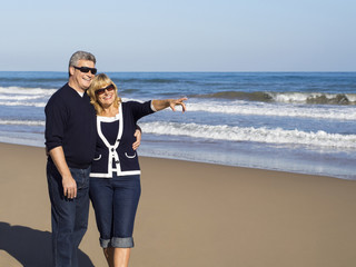 Happy mature couple points to on a sunny day at the beach