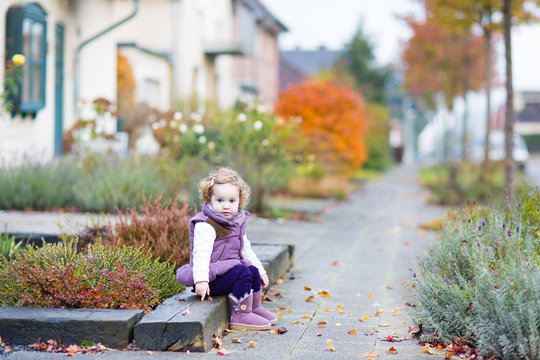 Little toddler girl with curly hair sitting on the front yard of