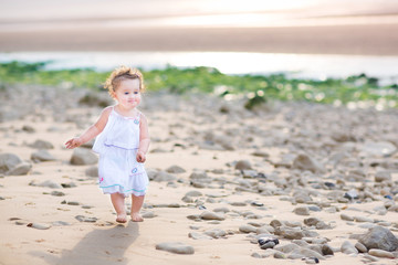 Funny toddler girl running at the beach at sunset wearing a whit