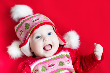 Happy laughing baby girl in a red dress with Christmas ornament