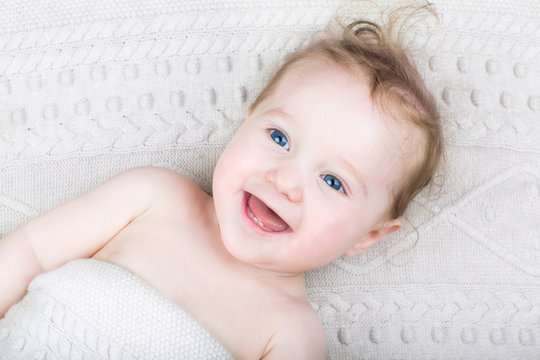 Cute laughing baby under a warm knitted blanket