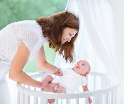 Young Mother Putting Her Newborn Baby Into A White Round Crib