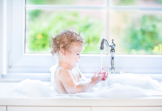 Funny baby girl playing with water and foam next to a big window
