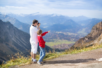 Young father and his teenager son taking pictures of a mountains