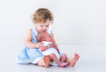 Toddler girl in a blue dress holding her newborn baby brother
