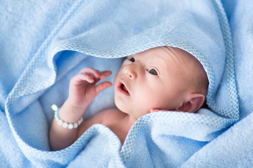 Funny newborn baby in a blue towel after bath