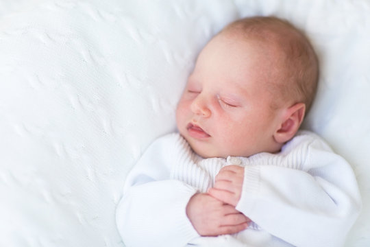 Sweet newborn baby sleeping on a white knitted blanket