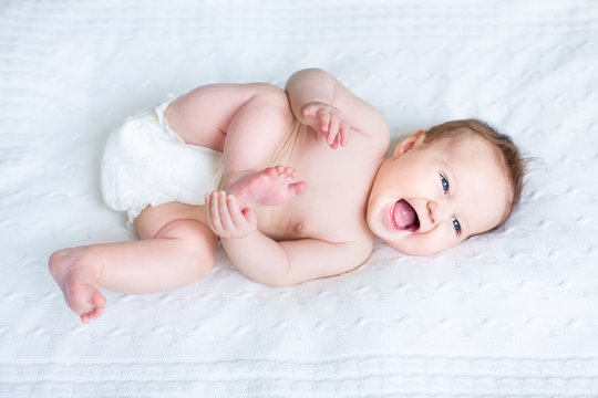Funny laughing baby wearing a diaper playing with her feet