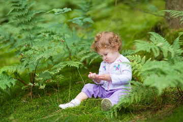 Funny curly baby girl eating wild raspberries in a autumn forest