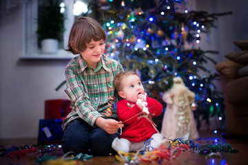 Little baby girl and her brother playing under Christmas tree