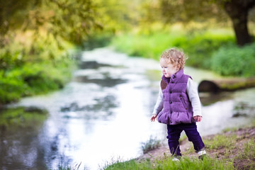 Little baby girl walking on a river shore in a nice autumn park