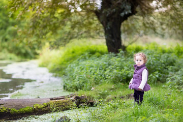 Naklejka na ściany i meble Cute baby girl playing at a river shore on a cold autumn day