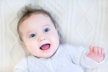 Happy laughing baby girl relaxing on a warm knitted blanket