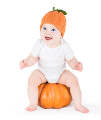 Funny laughing little baby sitting and playing on a huge pumpkin