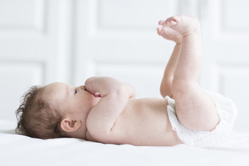 Funny baby girl relaxing in a diaper on a white blanket