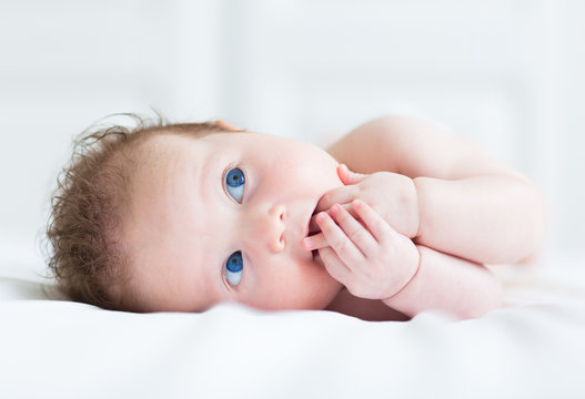 Portrait of a little baby with big blue eyes sucking own hand