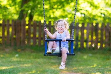 Laughing baby girl having fun on a swing ride at a playground