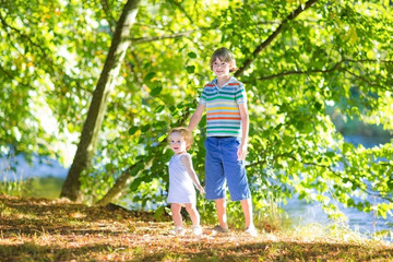 Fototapeta premium Cute school boy holding his baby sister playing at a river shore