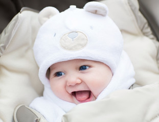 Funny laughing baby in a teddy bear hat sitting in a stroller