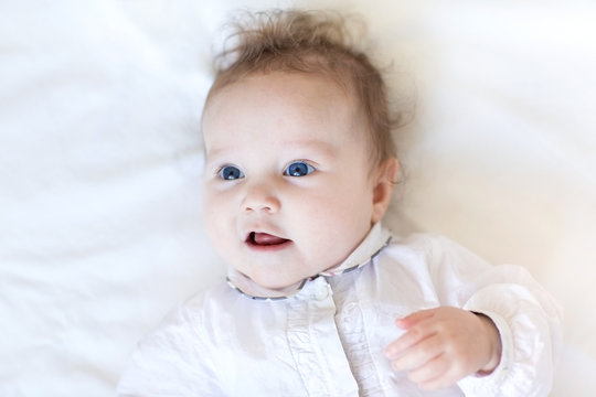 Beautiful little baby girl with big blue eyes on a white blanket