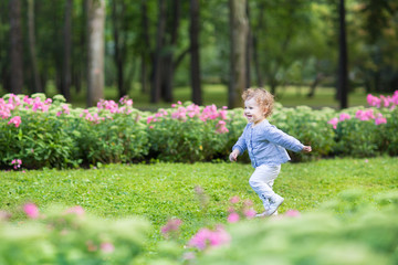Curly baby girl running in a beautiful park among pink flowers