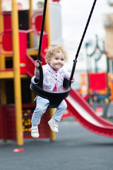 Happy smiling baby girl enjoying a swing ride on a playground