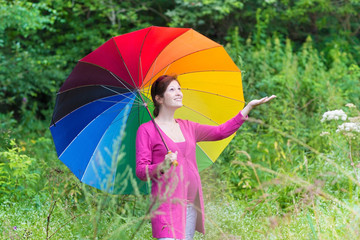 Attractive pregnant woman walking under a colorful umbrella