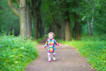 Cute baby girl in rubber rain boots walking in a rainy park