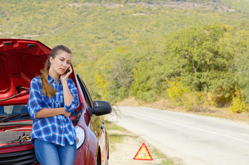 Young woman near broken car speaking by phone