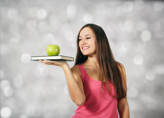 Young girl holds book and apple at light background