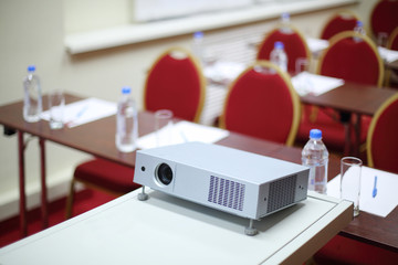Table with projector, tables and red chairs in room