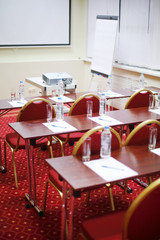 Tables with bottles, sheets,  pens, rows of chairs and projector